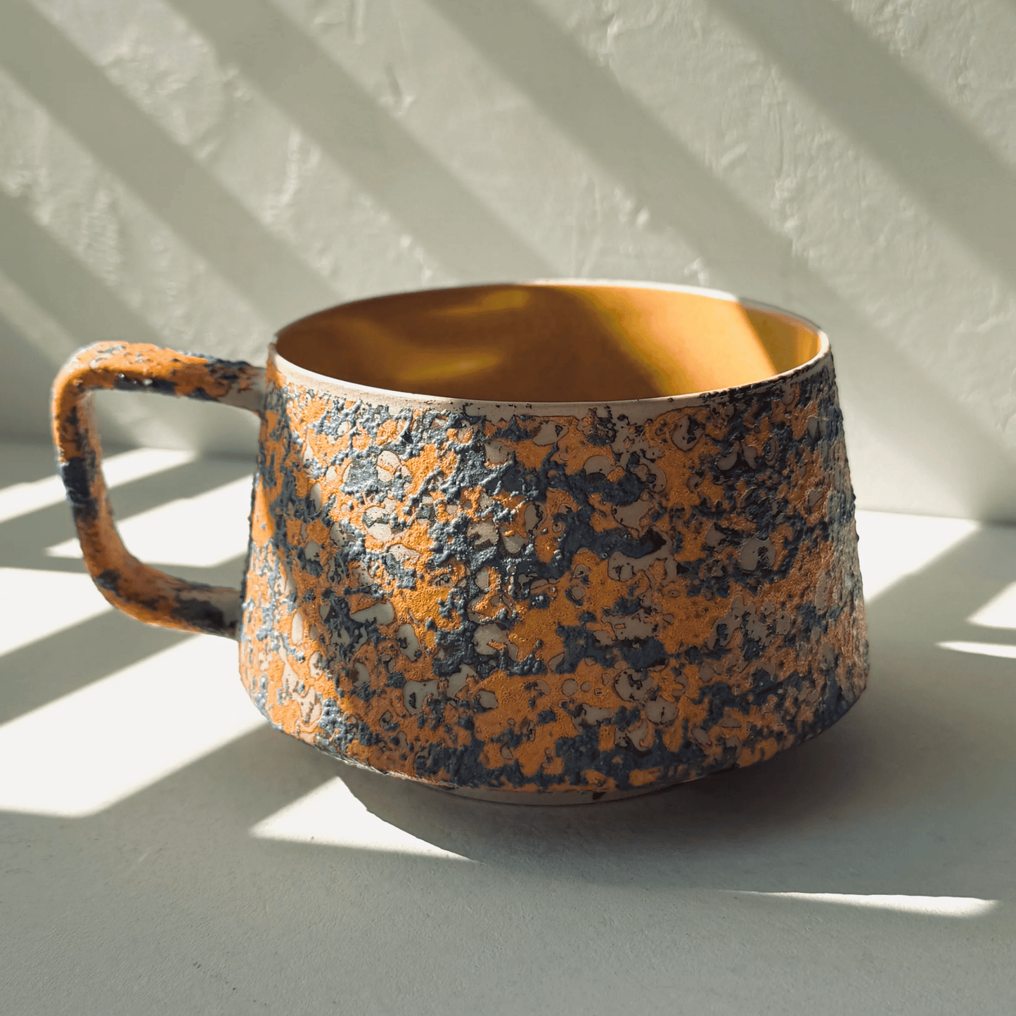 Ceramic mug with orange and black speckled pattern on a light background