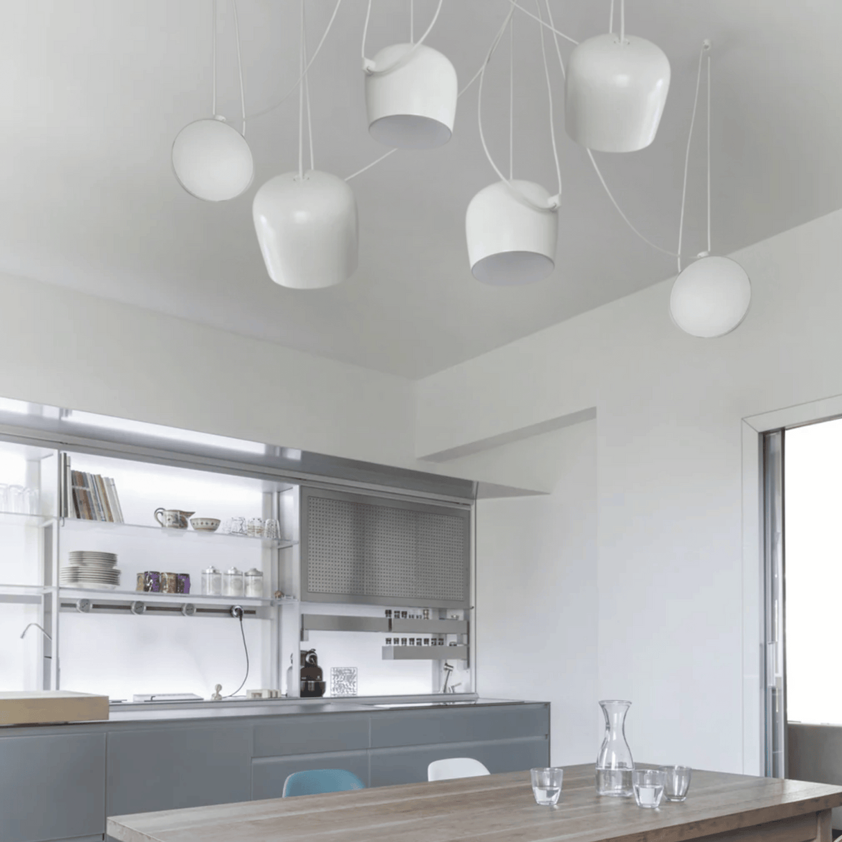 Modern kitchen with white pendant lights and a wooden dining table.