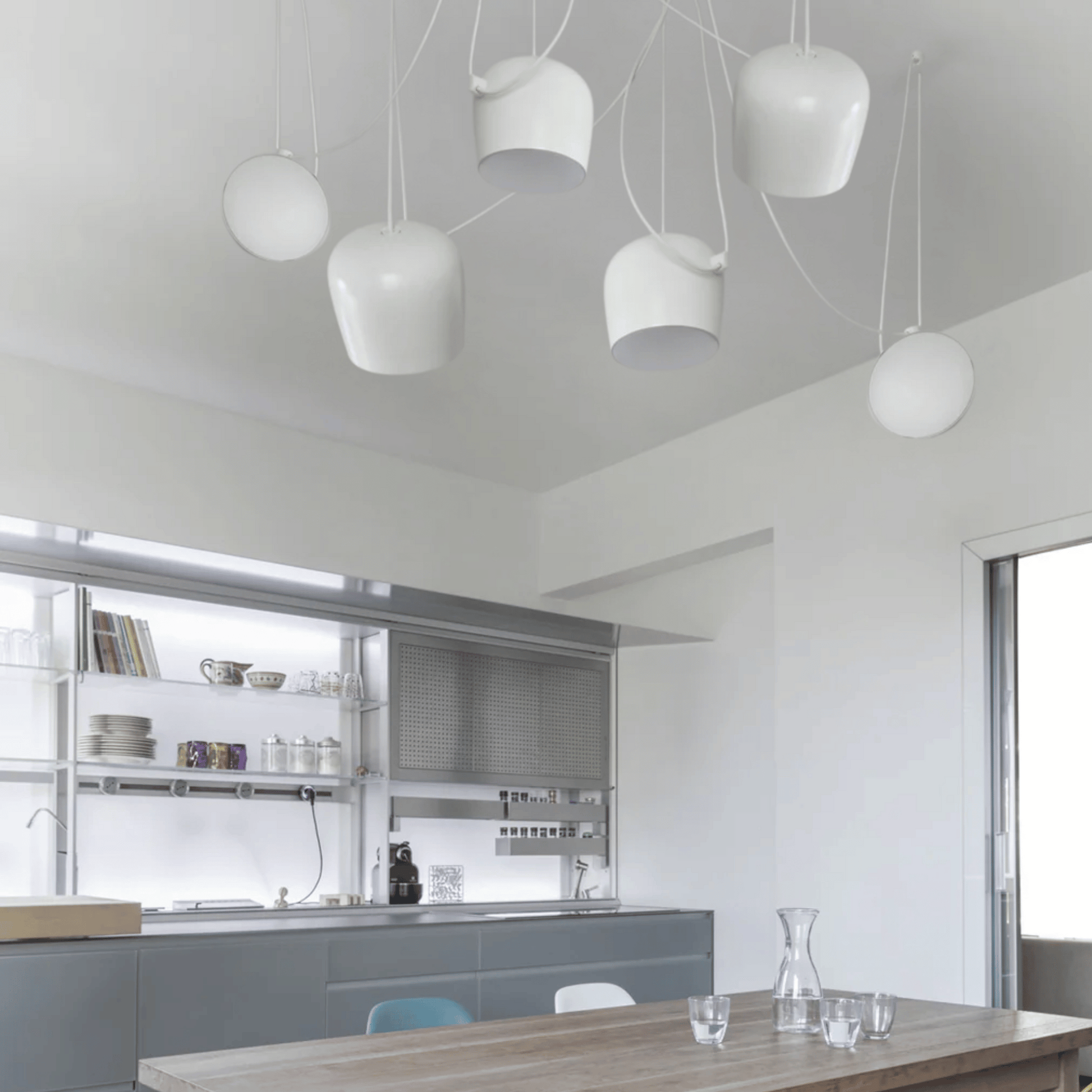Modern kitchen with white pendant lights and a wooden dining table.