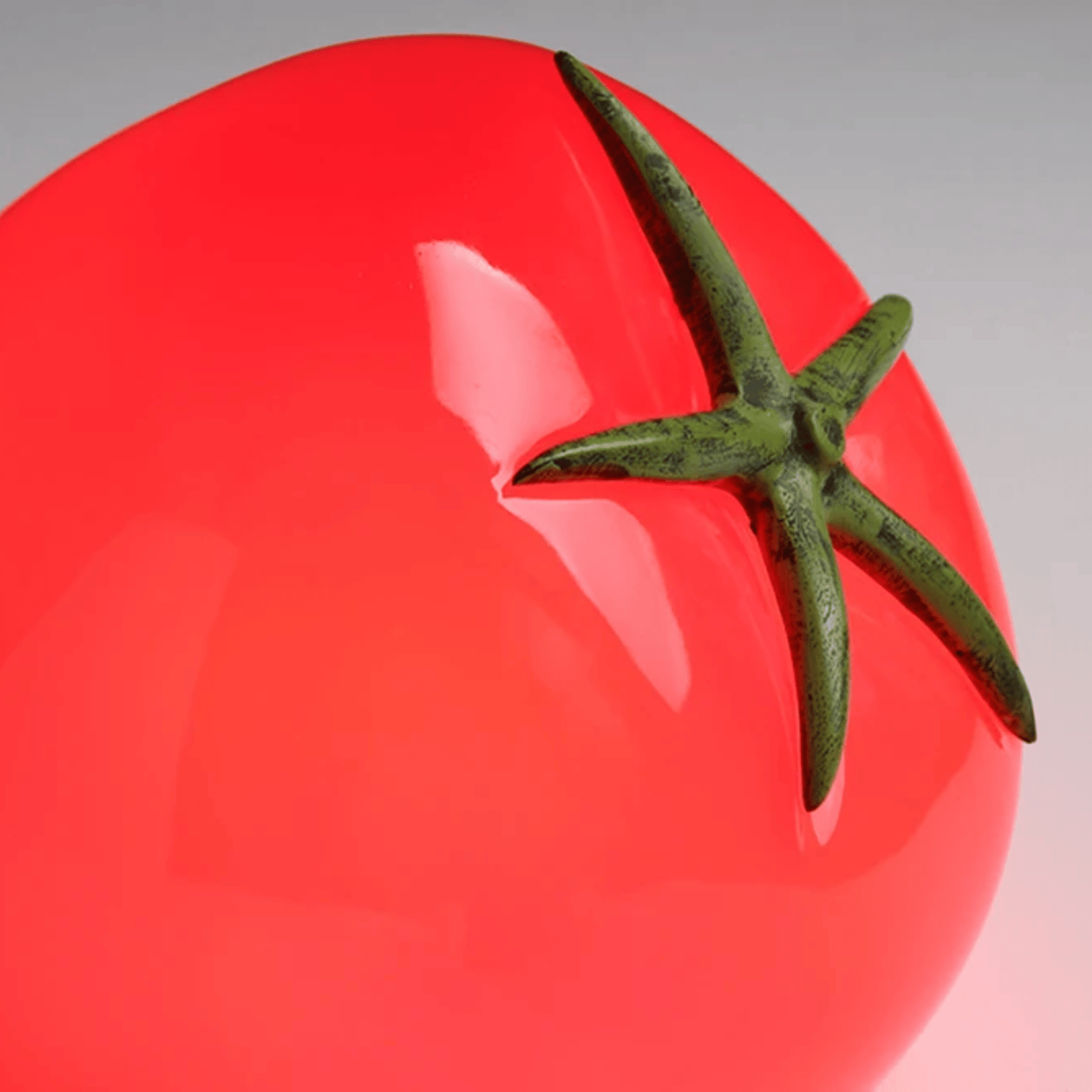 Close-up of a red tomato with a green stem on a reflective surface.