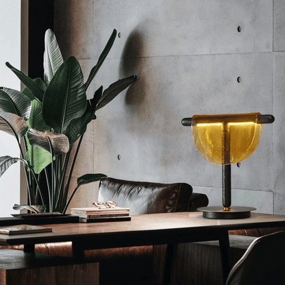 Modern interior with a table lamp, plant, and books against a concrete wall.