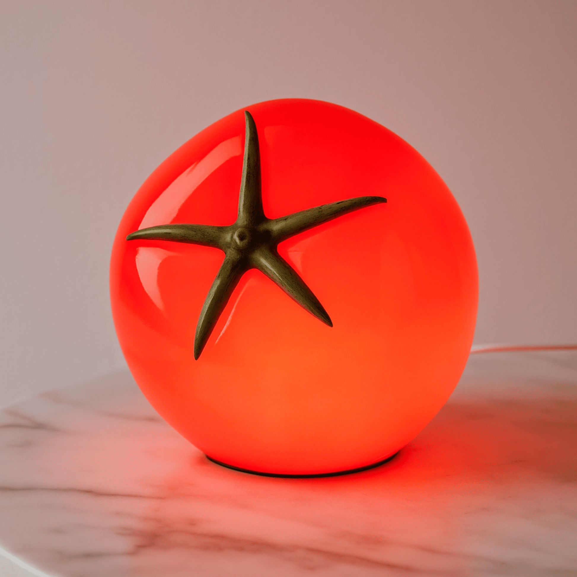 Glowing red tomato-shaped lamp on a marble surface with a neutral background