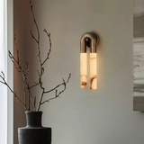 Wall-mounted light fixture with a vase containing branches on a neutral wall.