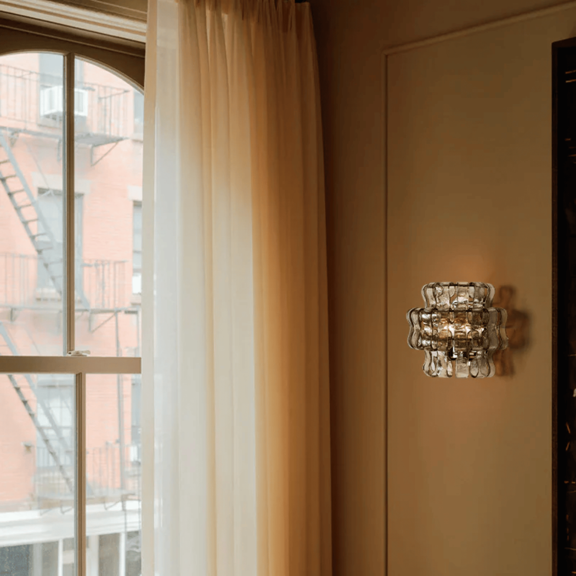 Decorative wall sconce on a beige wall next to a window with white curtains.