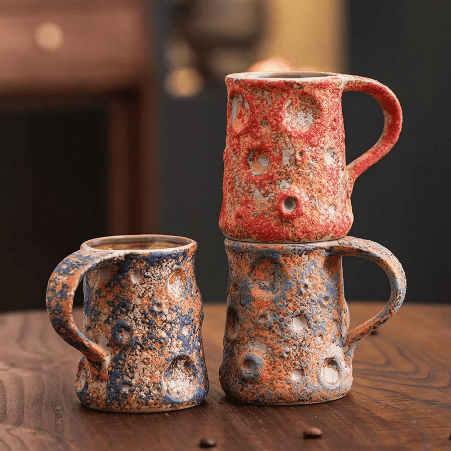 Three ceramic mugs with textured, multicolored glaze on a wooden surface.