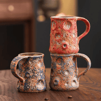 Three ceramic mugs with textured, multicolored glaze on a wooden surface.