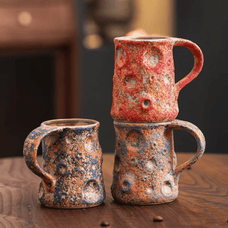 Three ceramic mugs with textured, multicolored glaze on a wooden surface.