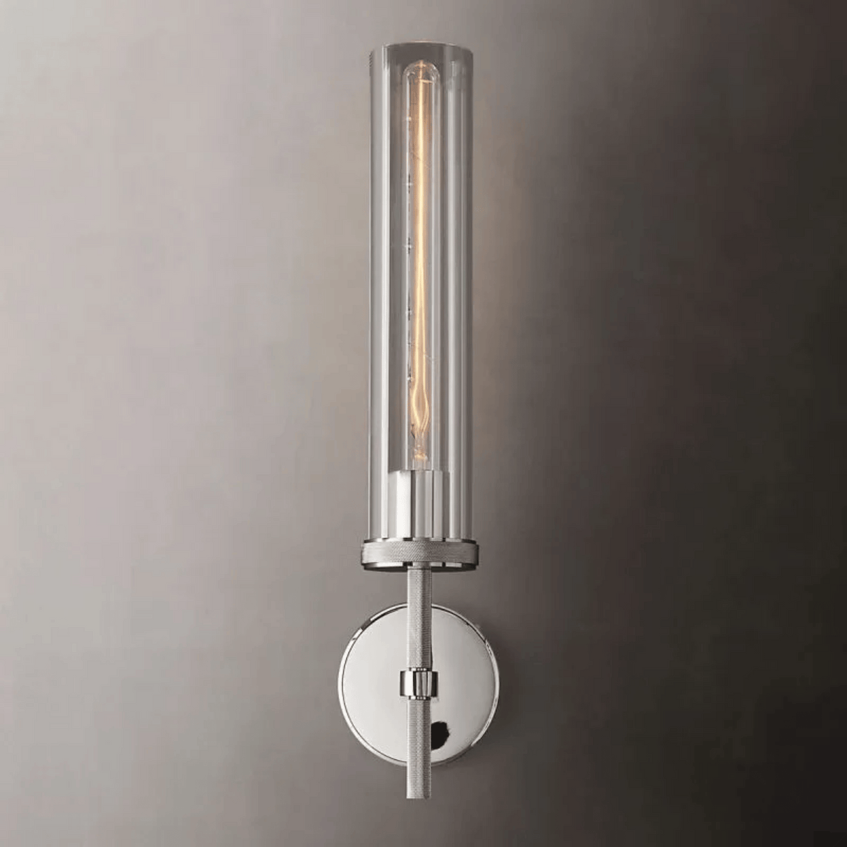 Wall-mounted cylindrical light fixture with clear glass cover on a gray wall.