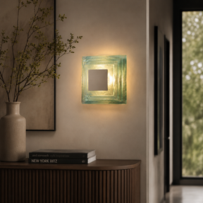 Square wall light fixture on a neutral wall with a vase and books on a wooden surface.