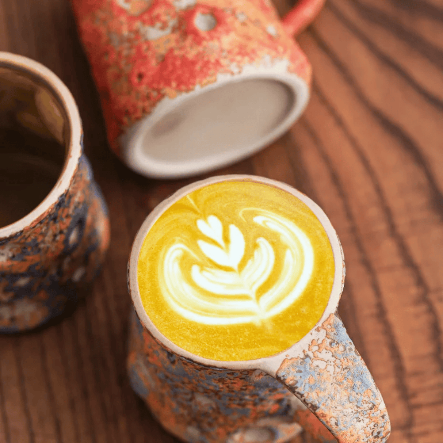Ceramic mug with colorful glaze pattern containing a latte art design on a wooden surface.
