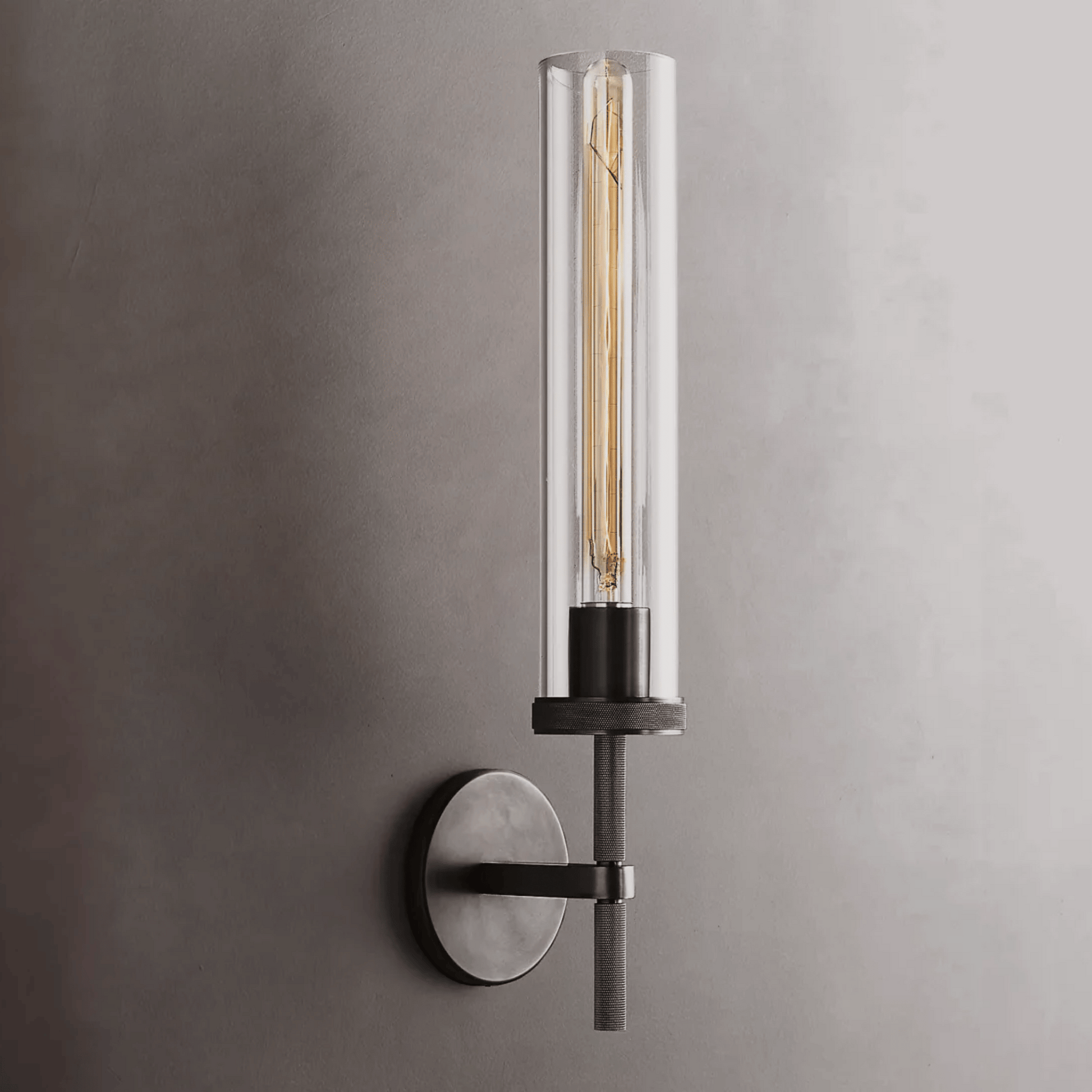 Modern wall-mounted light fixture with clear cylindrical glass shade on a gray background