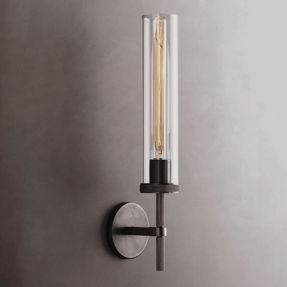 Modern wall-mounted light fixture with clear cylindrical glass shade on a gray background