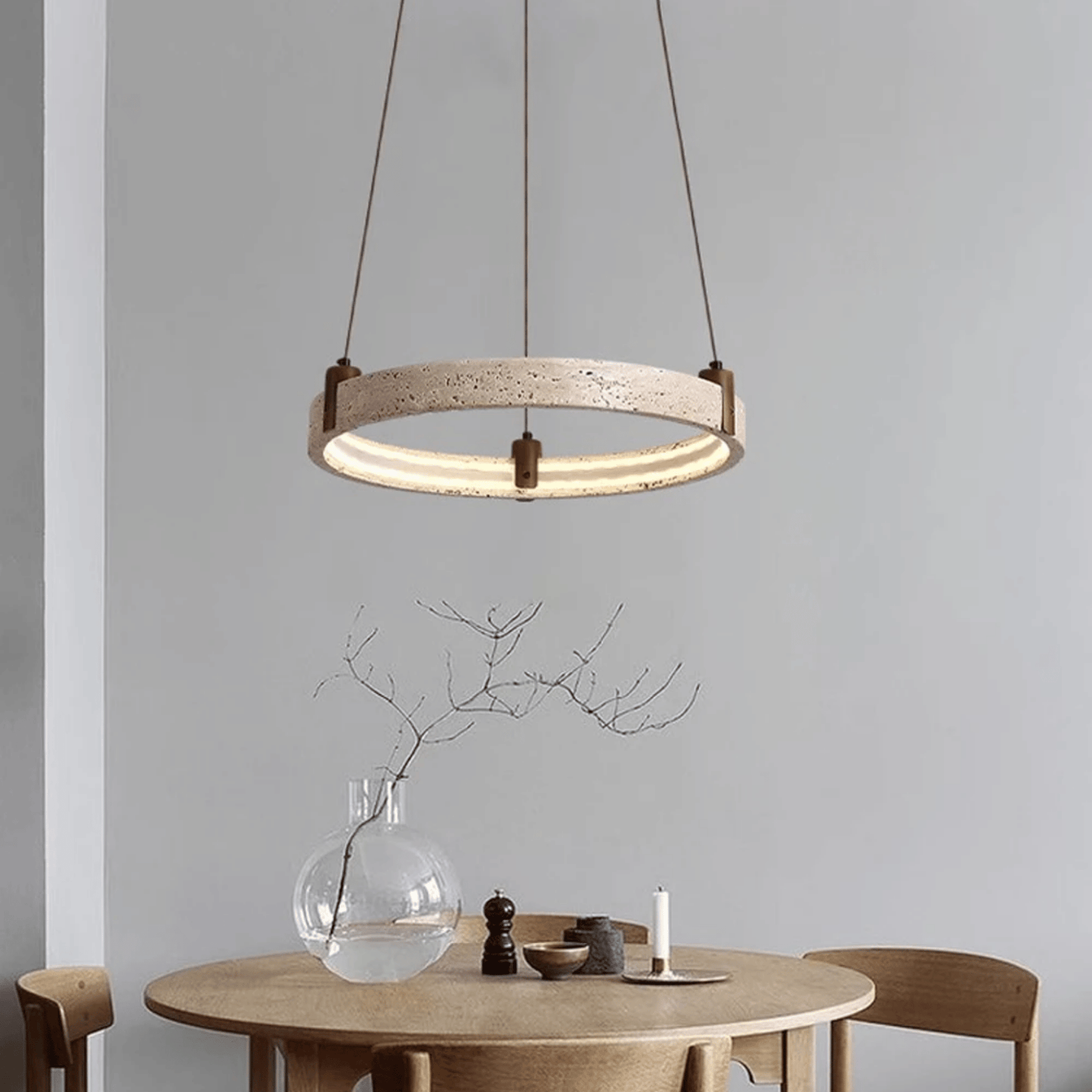 Modern pendant light hanging above a dining table with a vase and candle on a neutral background