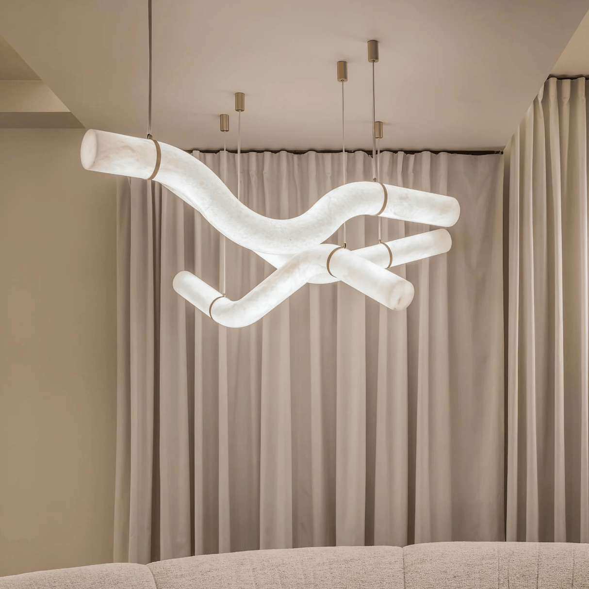 Modern chandelier hanging above a sofa with beige curtains in the background