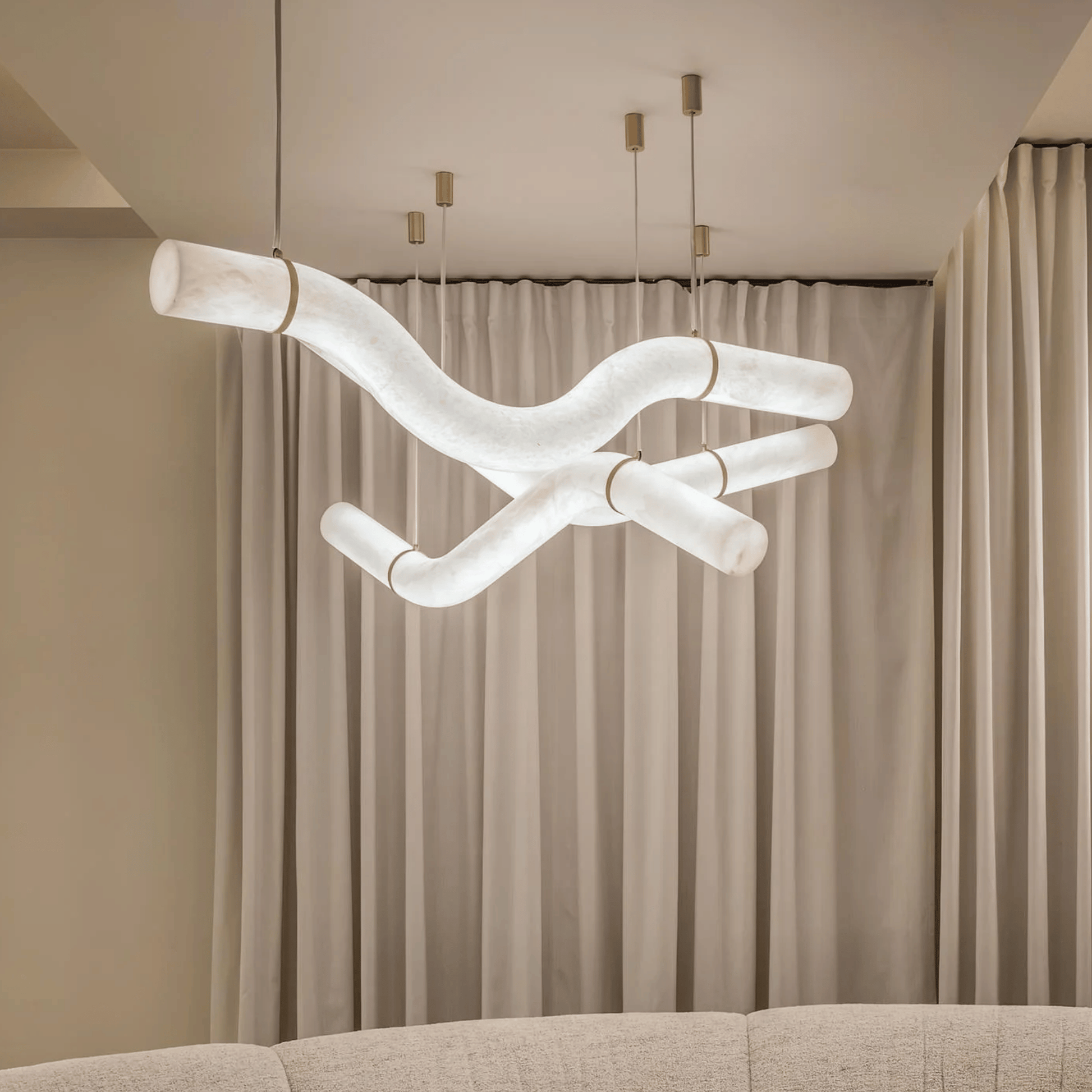 Modern chandelier hanging above a sofa with beige curtains in the background