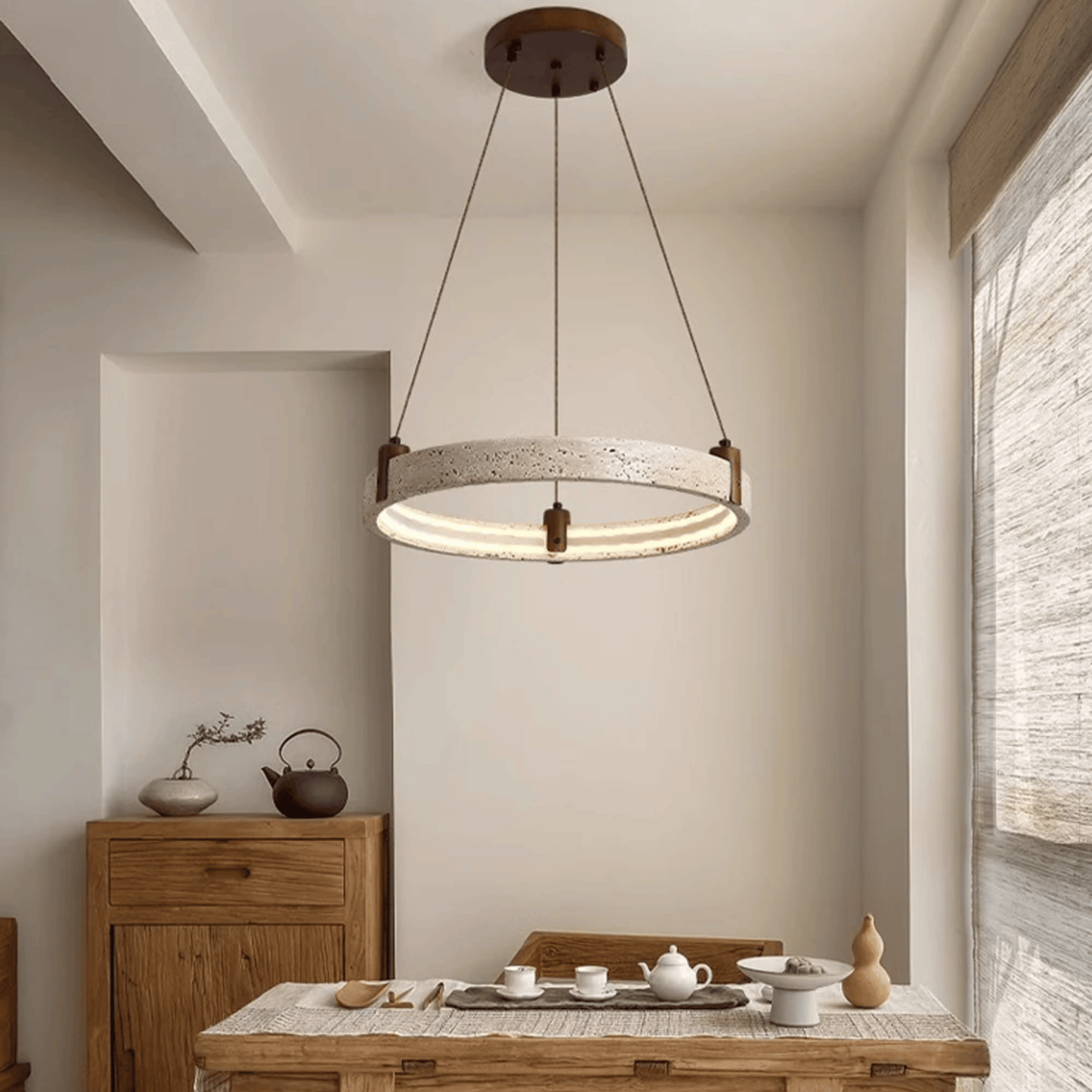 Modern pendant light hanging above a dining table with tea set in a room with wooden furniture and a window.
