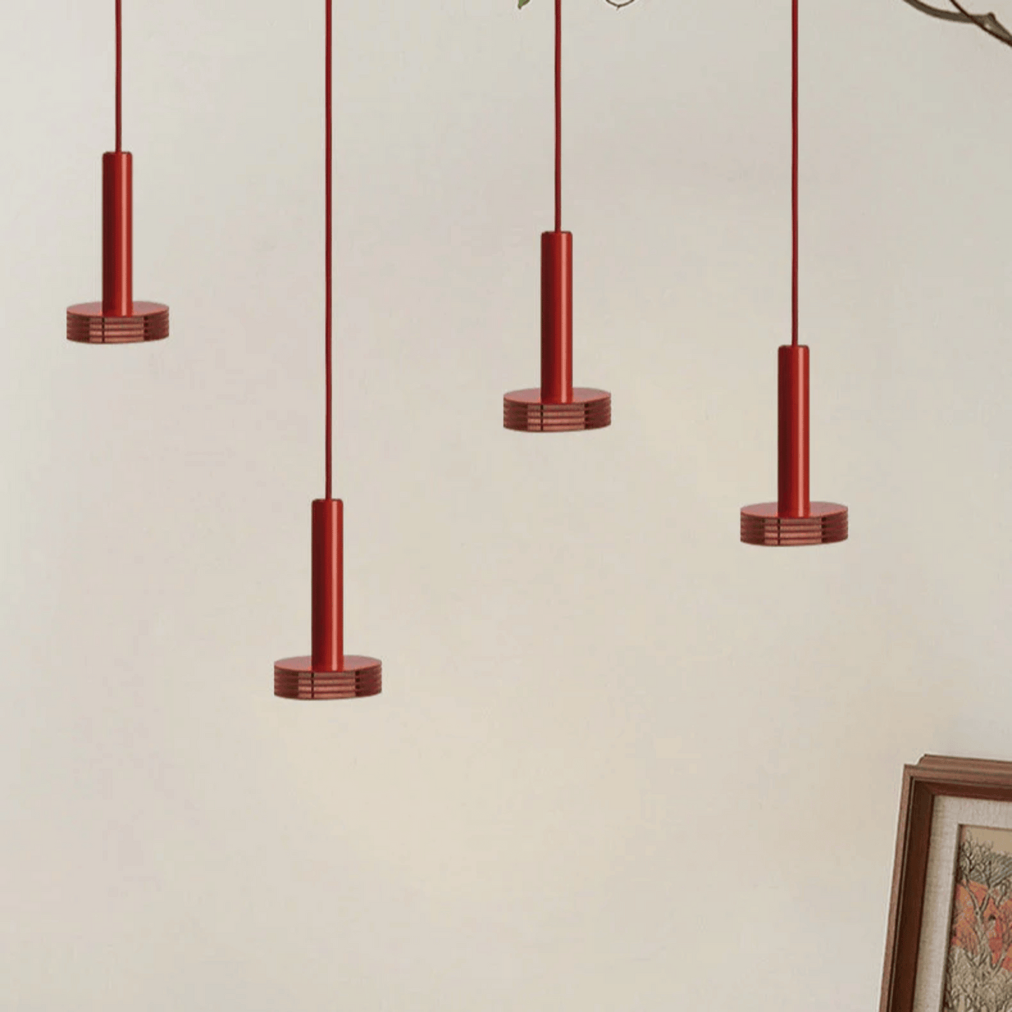 Four red pendant lights hanging against a beige wall with a framed picture on the right.