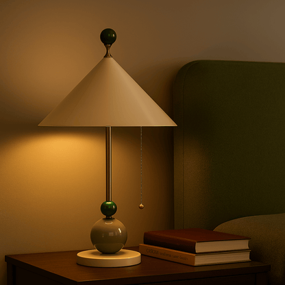 Table lamp with a beige shade and green base on a wooden surface, with books in the background.