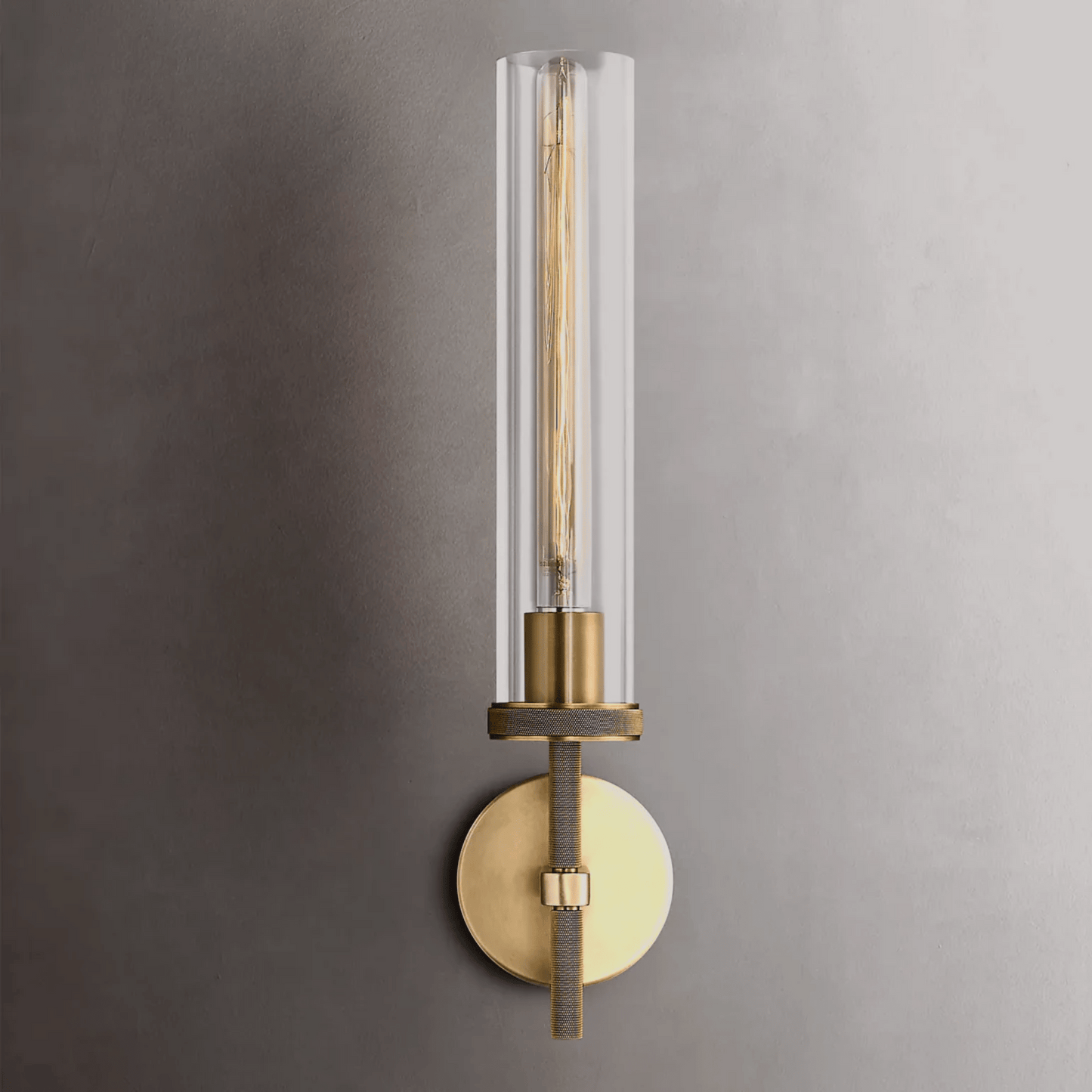 Modern wall sconce with clear glass shade and brass finish on a gray wall.