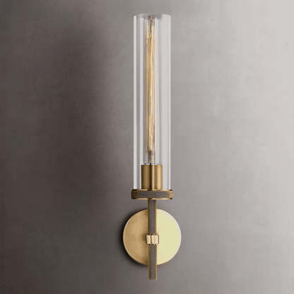 Modern wall sconce with clear glass shade and brass finish on a gray wall.