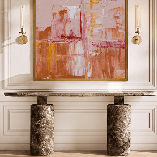 Abstract painting on a wall above a marble console table with sconces on either side.