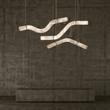 Modern chandelier with curved design hanging against a textured wall.