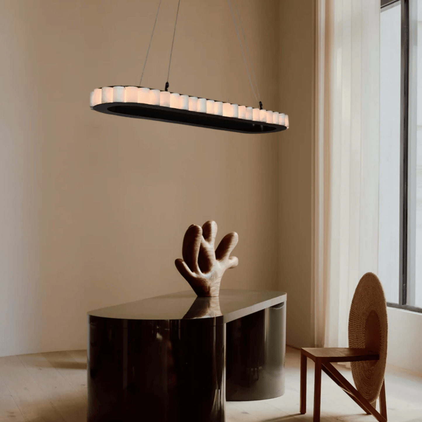 Modern pendant light hanging above a table with a sculpture in a minimalistic room.