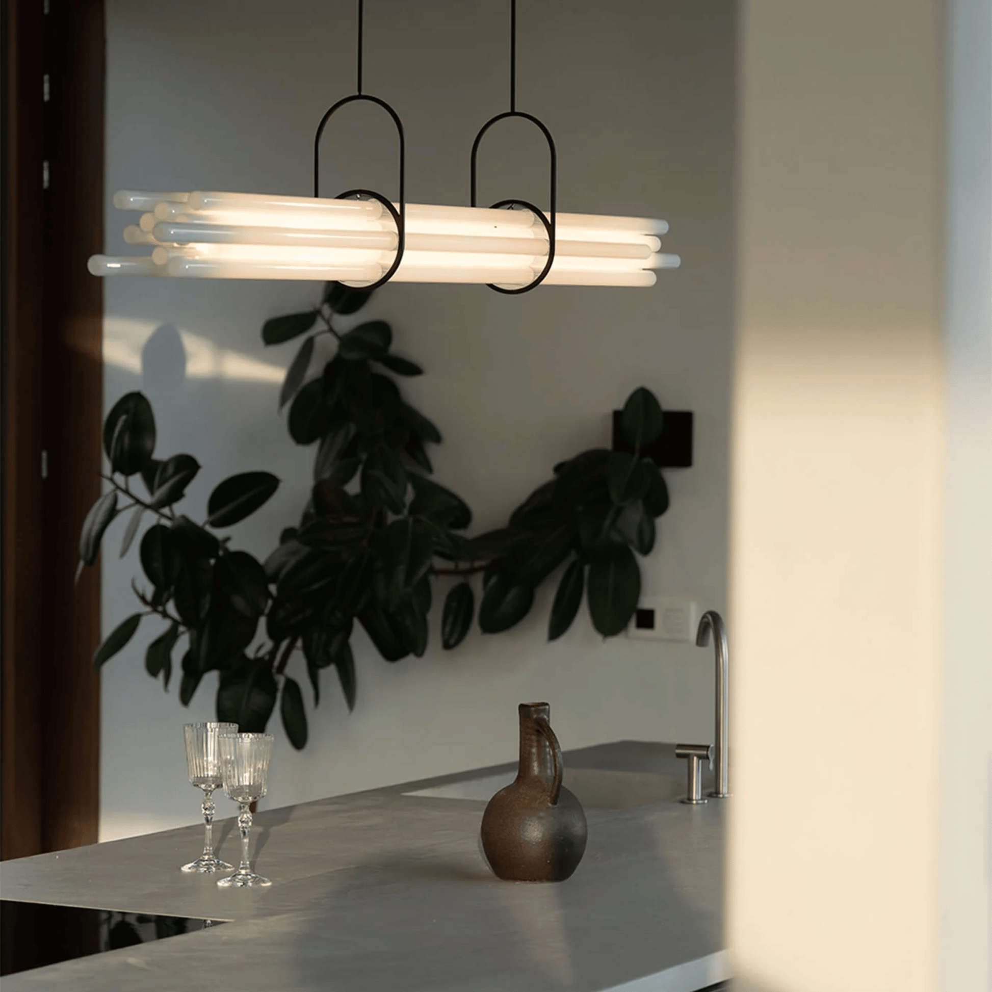 Modern pendant light fixture in a room with a plant and decorative items on a table.