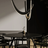 Modern dining room with a black round table and chairs, featuring a unique ceiling light fixture.
