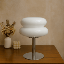 Modern white stool with a metallic base on a wooden surface against a beige wall.