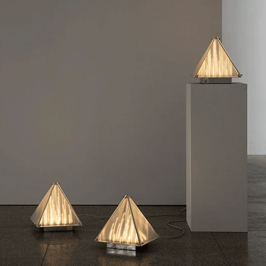 Three pyramid-shaped lamps on a dark floor with a plain wall background