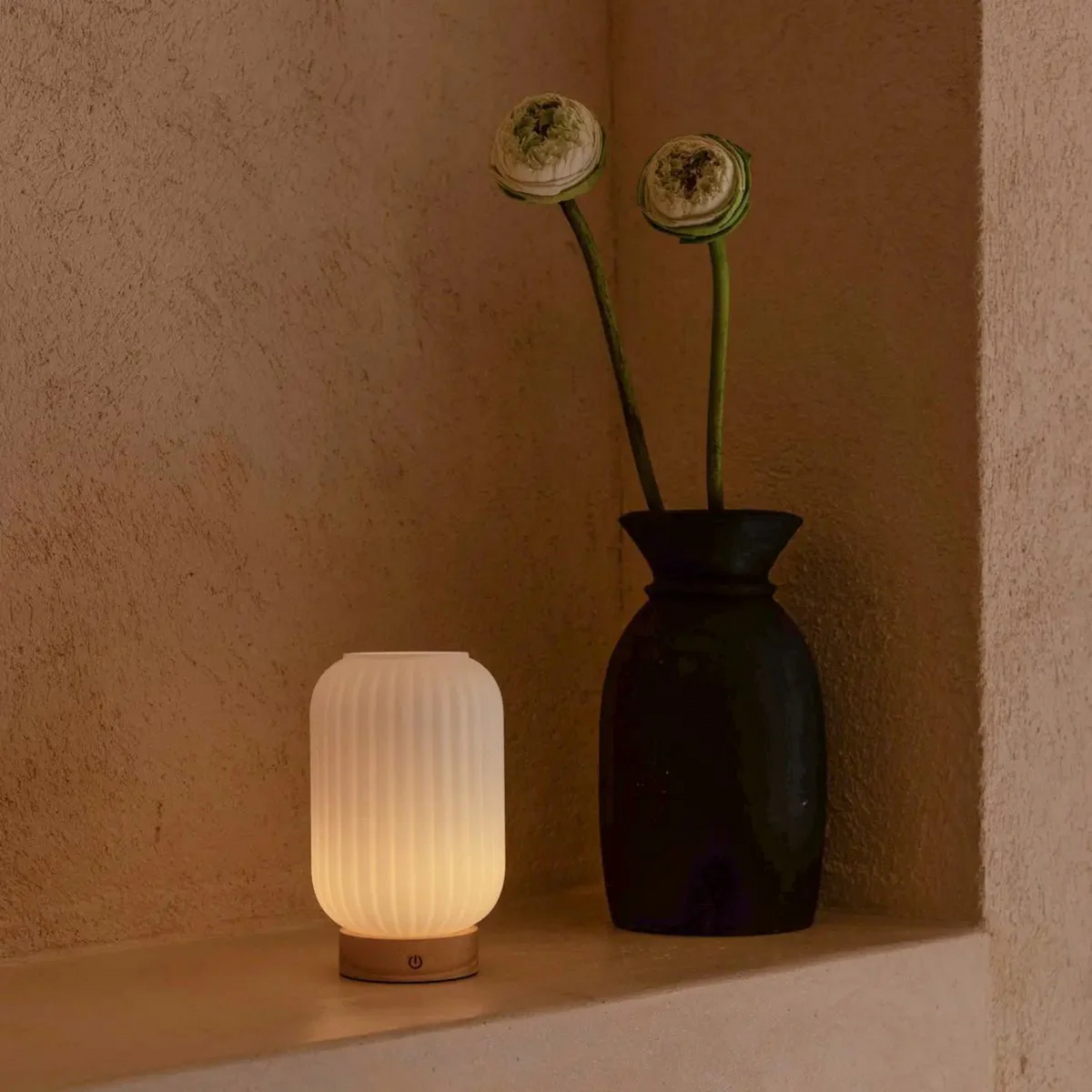 Small lamp with a black vase and flowers against a beige wall