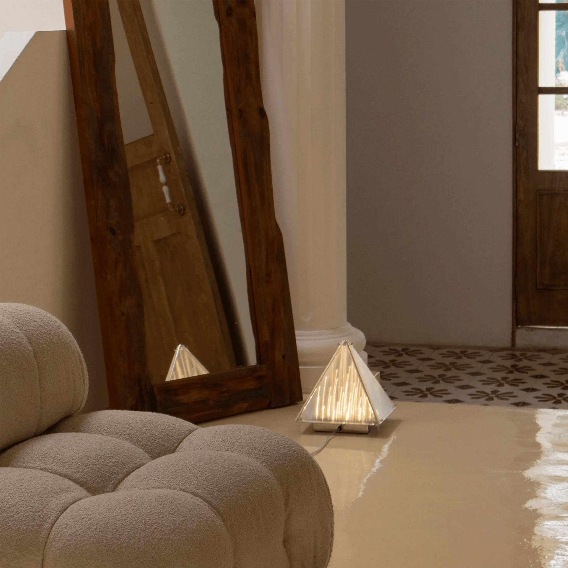 Pyramidal lamp on a floor next to a textured wall and wooden door.