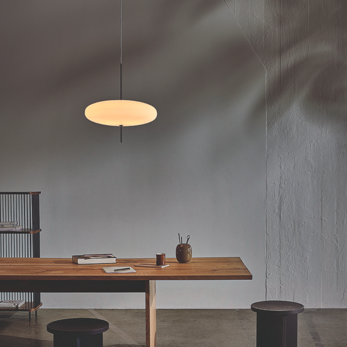 Modern pendant light hanging above a wooden table with minimal decor in a room with gray walls.