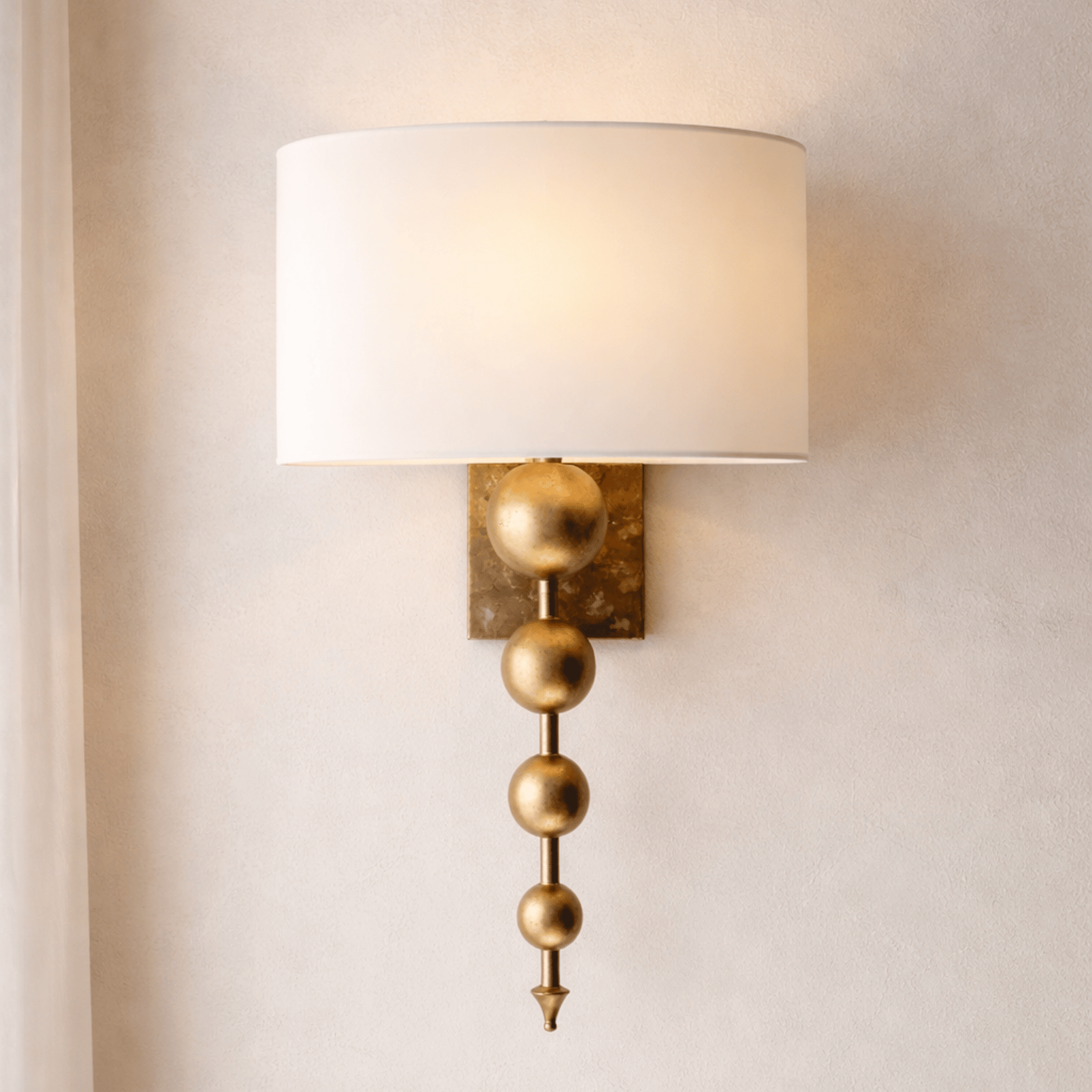 Wall sconce with gold decorative elements and a white lampshade on a neutral wall.