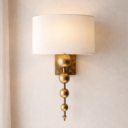 Wall sconce with gold decorative elements and a white lampshade on a neutral wall.