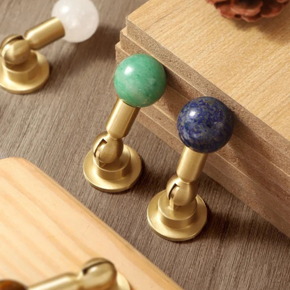 Assorted brass knob handles with various gemstone spheres including brown, blue, green, and pink.