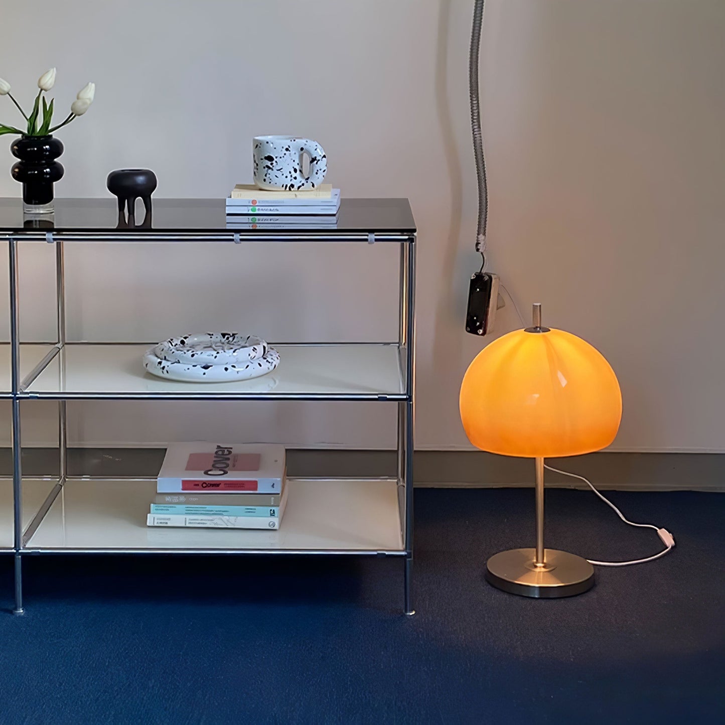 A stylish orange  globe-shaped lamp placed on a desk, with a view of city buildings visible through the window in the background.