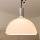 A close-up shot of a dome-shaped pendant light with a warm glowing white shade and a metallic top mount.