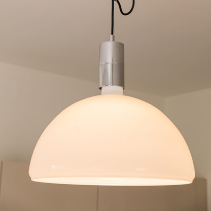 A close-up shot of a dome-shaped pendant light with a warm glowing white shade and a metallic top mount.