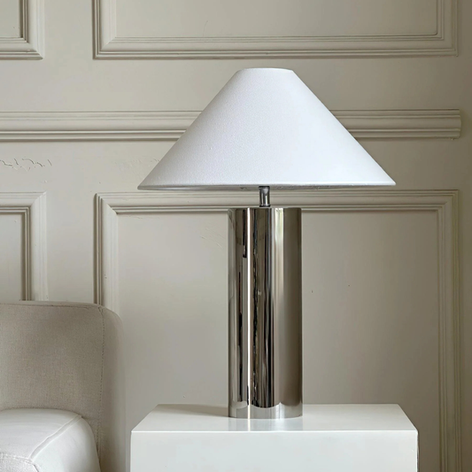 modern chrome table lamp with a white cone lampshade placed on a white cabinet
