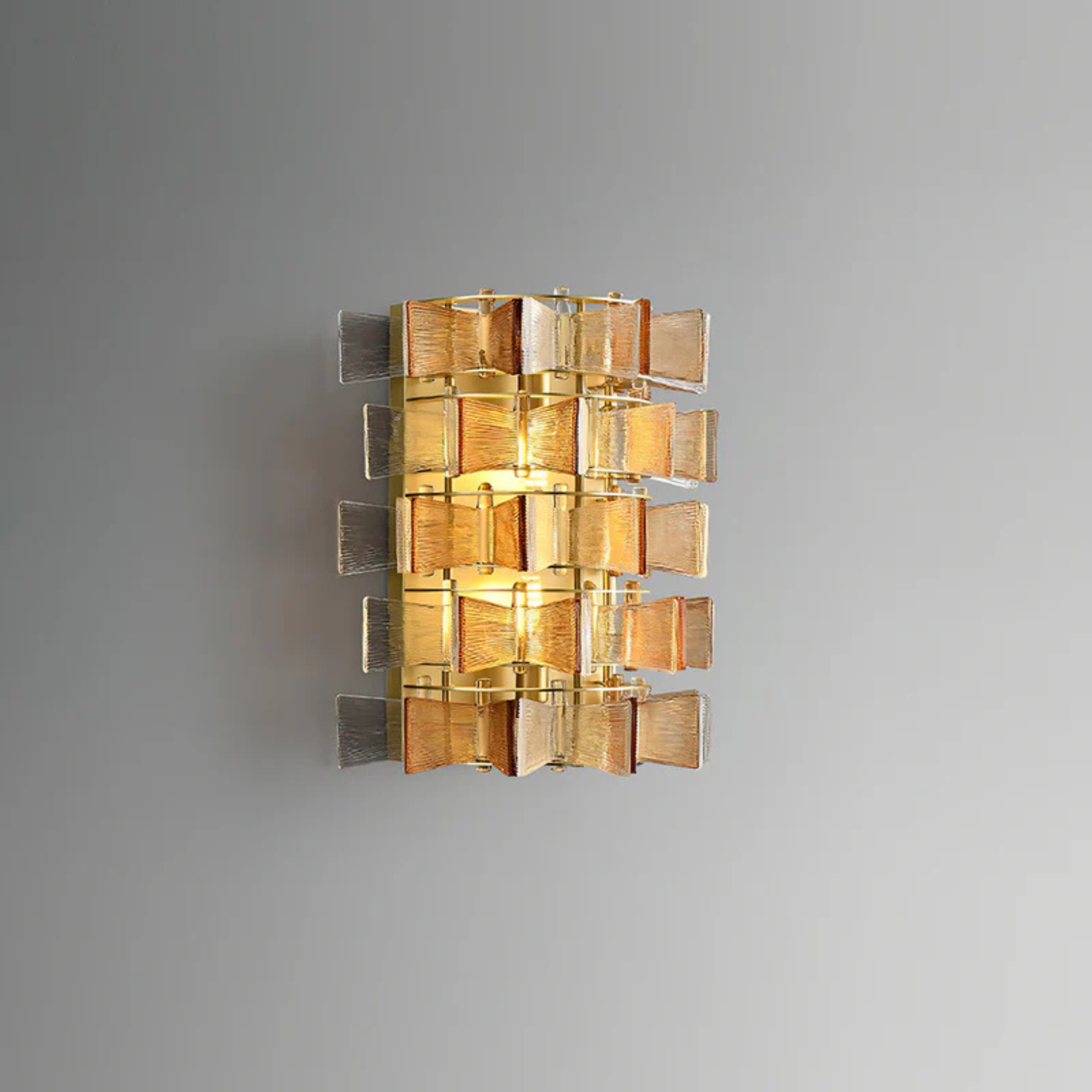 Wall-mounted golden light fixture made of stacked ribbed glass blocks glowing warmly on a gray wall.