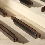 Several sleek bronze handles with wooden inserts placed neatly on a cream-colored surface.