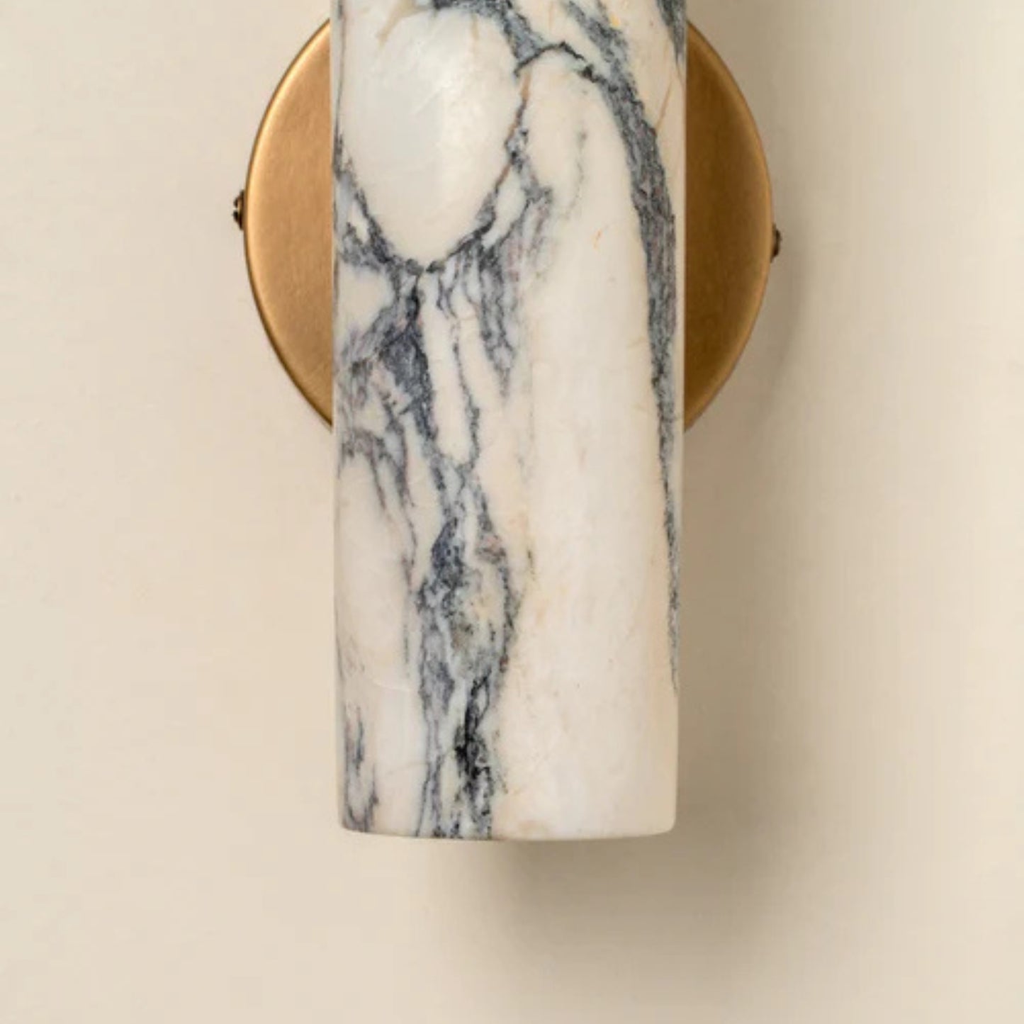 Side view of a sculptural marble and brass wall sconce emitting soft warm light.