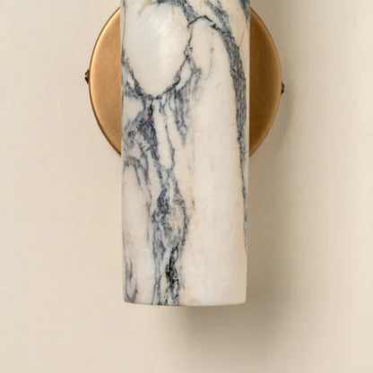 Side view of a sculptural marble and brass wall sconce emitting soft warm light.