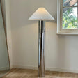 tall chrome floor lamp with a wide cone-shaped white lampshade placed beside a window