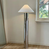 tall chrome floor lamp with a wide cone-shaped white lampshade placed beside a window