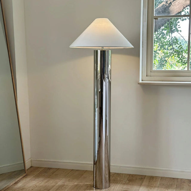 tall chrome floor lamp with a wide cone-shaped white lampshade placed beside a window