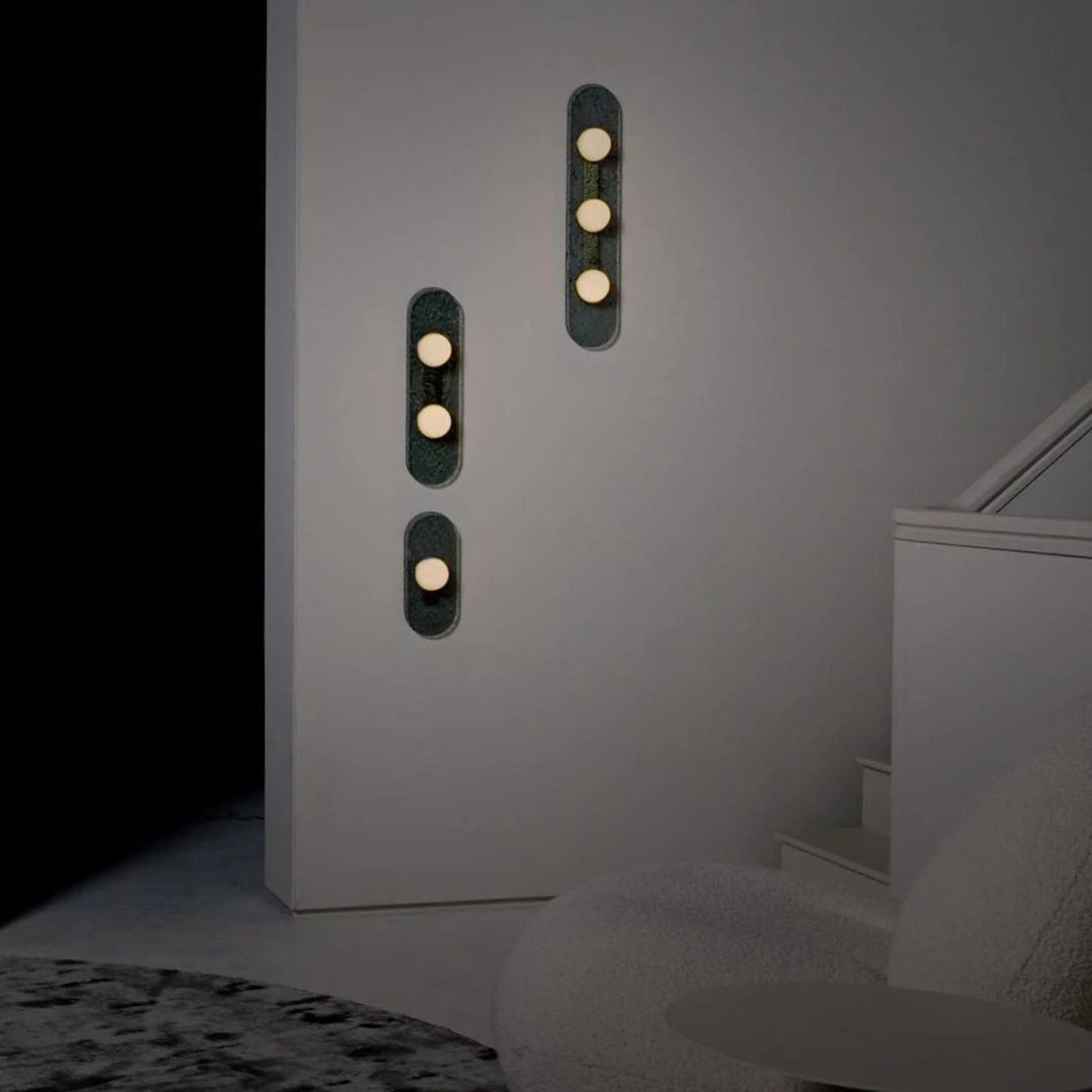 vertical grey wall sconce with three round warm white bulbs arranged in a straight line on a textured elongated backplate