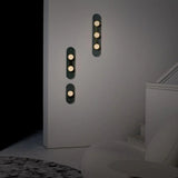 vertical grey wall sconce with three round warm white bulbs arranged in a straight line on a textured elongated backplate